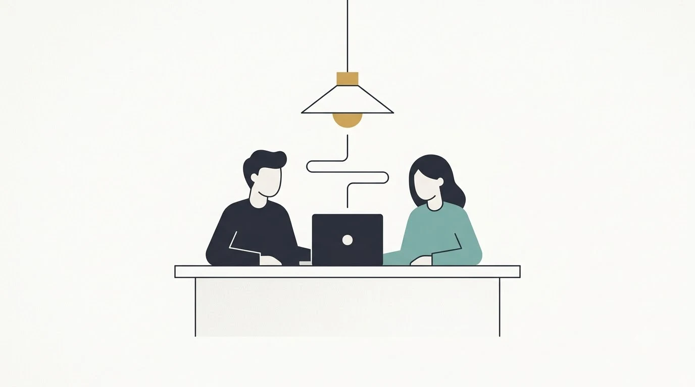 Two figures sitting side by side at a desk and working on one shared laptop.