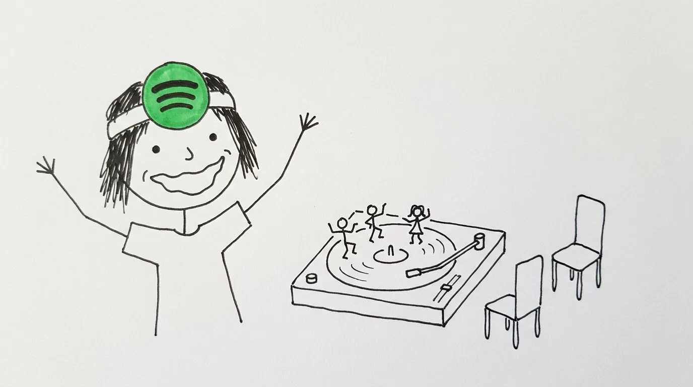 A delighted person watches four tiny performers dance on a turntable beside interview chairs.
